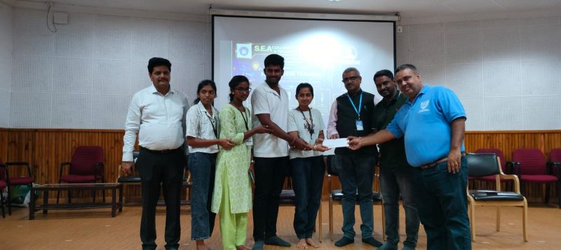 A student team receiving a prize envelope on stage at SEA College